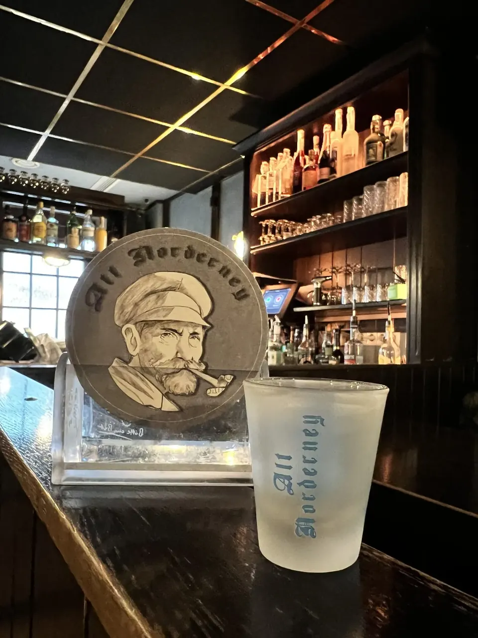 Schnapsglas mit Logo der Kneipe auf dem Tresen